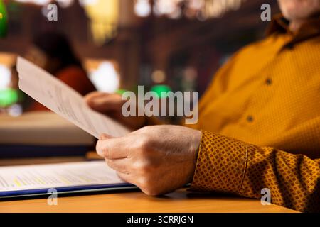 Uomo anziano studente maturo in biblioteca che impara per i suoi studi, circondato da materiali accademici e libri. L'allievo si concentra sulla ricerca e lo studio, abbracciando l'intelligenza in età avanzata. Foto Stock