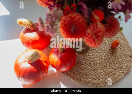 Decorazioni degli interni autunnali. Piccole zucche arancioni messe sul tavolo con fiori d'autunno pieni di dalie arancioni. Vista dall'alto. Primo piano di verdure Foto Stock
