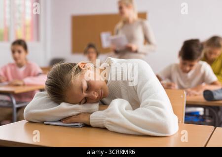 Ragazza della scuola che si trova e dorme alla scrivania Foto Stock