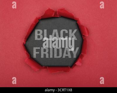 Un buco strappato in carta rossa che rivela uno sfondo grigio con le parole "Black Friday". Concetto di materiale pubblicitario e di marketing. Foto Stock