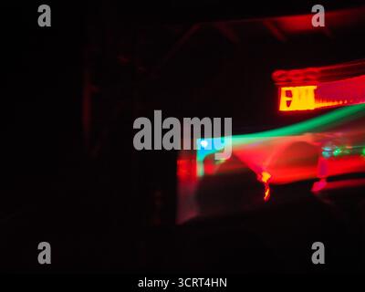 Percorsi di luce astratta all'interno di un club burlesque buio a Brooklyn, New York, con un cartello rosso di uscita e riflessi colorati al neon Foto Stock
