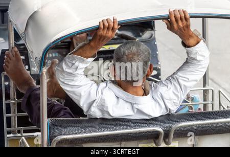 Un autista più anziano siede sui sedili posteriori di un triciclo tradizionale e aspetta i passeggeri, Bangkok, Thailandia Foto Stock
