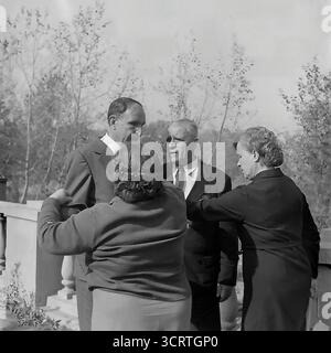 Un'autentica fotografia d'archivio in bianco e nero del 1960 mostra un gruppo di funzionari e un veterano di guerra decorato a Sviatohirsk (allora Slavyanogorsk), RSS Ucraina. L'incontro si svolge su una terrazza all'aperto di un sanatorio o una "casa di riposo" nella famosa località turistica. Gli uomini e le donne sono impegnati in una conversazione rilassata ma formale. La presenza di un veterano della grande Guerra Patriottica (seconda guerra mondiale), la sua tuta decorata con medaglie, indica un evento ufficiale o commemorativo. Si tratta di un sincero assaggio della vita sociale delle figure rispettate dell'Unione Sovietica Foto Stock
