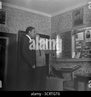 Una fotografia d'archivio in bianco e nero degli anni '1960, scattata all'interno del "Museo della Gloria rivoluzionaria, militare e del lavoro" a Sviatohirsk, RSS Ucraina. Un veterano sovietico decorato della grande Guerra Patriottica (seconda guerra mondiale) funge da guida, spiegando una mostra a un funzionario. Egli punta a una mappa che descrive dettagliatamente le operazioni militari per la liberazione del Donbas. Si tratta di una scena potente e candida di un eroe di guerra che funge da testimone vivente, trasmettendo la memoria storica all'interno di un museo di epoca sovietica Foto Stock