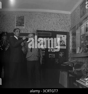 Una fotografia d'archivio in bianco e nero degli anni '1960, scattata all'interno del "Museo della Gloria rivoluzionaria, militare e del lavoro" a Sviatohirsk, RSS Ucraina. Un veterano sovietico decorato della grande Guerra Patriottica (seconda guerra mondiale) funge da guida, spiegando una mostra a un funzionario. Egli punta a una mappa che descrive dettagliatamente le operazioni militari per la liberazione del Donbas. Si tratta di una scena potente e candida di un eroe di guerra che funge da testimone vivente, trasmettendo la memoria storica all'interno di un museo di epoca sovietica Foto Stock