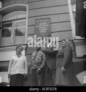 Un'autentica fotografia d'archivio in bianco e nero del 1960, che mostra un gruppo di persone all'ingresso di un museo locale a Sviatohirsk (allora Slavyanogorsk), RSS Ucraina. Il cartello sull'edificio riporta "Museo della Gloria rivoluzionaria, militare e del lavoro", un nome tipico per un'istituzione storica dell'epoca sovietica. Il gruppo, che include un veterano di guerra decorato, un funzionario e altri visitatori, è riunito sotto il cartello. Si tratta di una classica istantanea della vita culturale e ideologica in una città provinciale dell'URSS Foto Stock