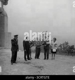 Una suggestiva fotografia d'archivio in bianco e nero degli anni '1960 mostra una delegazione ufficiale che visita il colossale Monumento ad Artem a Sviatohirsk, RSS Ucraina. Il gruppo, che include funzionari del partito e veterani di guerra decorati, cammina alla base della statua gigante. Progettato da Ivan Kavaleridze, il monumento è un capolavoro di arte sovietica famoso in tutto il mondo, eseguito in uno stile cubista/costruttivista unico. Questa immagine cattura un pellegrinaggio ufficiale verso uno dei monumenti ideologici più significativi della regione del Donbas e dell'intera URSS Foto Stock