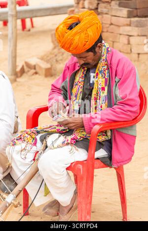 Rajasthani Man in vibrante abbigliamento tradizionale contando la valuta accanto allo strumento Folk nel Desert Village, Pushkar, India, 28 gennaio 2024 Foto Stock
