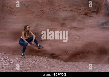 Giovane donna seduta contro un muro di arenaria rossa in un canyon del deserto Foto Stock