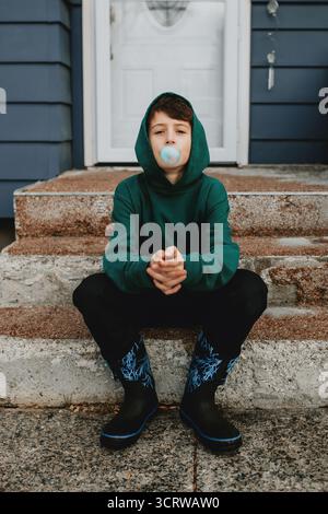 Ragazzo che fa soffiare gomma da bolla sui gradini anteriori Foto Stock