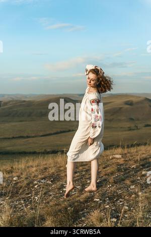Una donna in abito nazionale si trova sullo sfondo delle colline Foto Stock