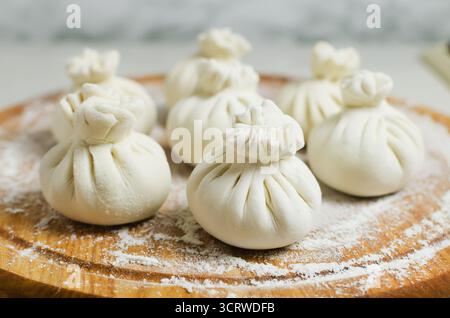 Khinkali crudi su un tagliere con farina su un tagliere rotondo sul tavolo. Concetto di cucina tradizionale georgiana. Orientamento orizzontale. SEL Foto Stock