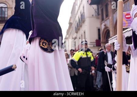 L'agente di polizia interagisce con la folla mentre i penitenti passano durante le processioni della settimana Santa a Siviglia, Spagna. Foto Stock