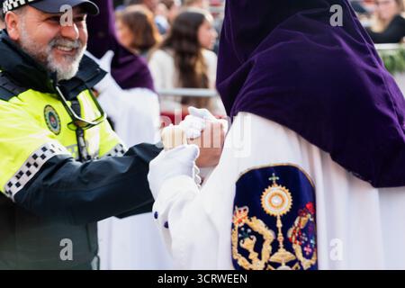 L'agente di polizia interagisce con un penitente durante le processioni della settimana Santa a Siviglia, Spagna. Foto Stock
