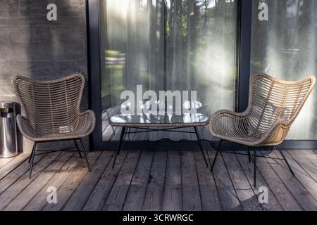 Questa immagine mostra un elegante spazio esterno caratterizzato da due sedie in rattan e un contemporaneo tavolo in vetro, invitante tranquillità e relax mentre si diverte Foto Stock