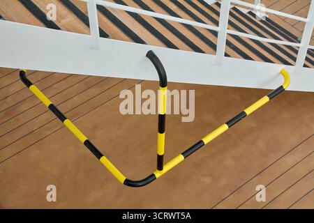 Una barriera di sicurezza con strisce gialle e nere crea uno schema geometrico sul ponte di una nave, che funge da segnale visivo di avvertimento e di guida. Foto Stock