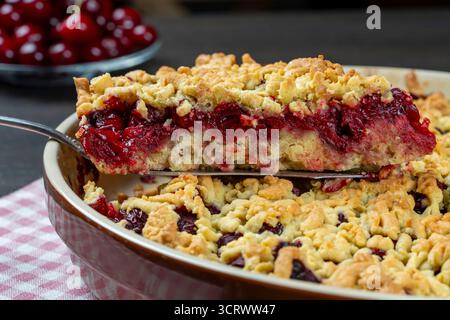 Piatto da forno con gustosa torta di ciliegie, primo piano. Deliziosa torta fatta in casa con ciliegie rosse fresche su un tavolo di legno. Torta estiva con crosta corta e frutti di bosco Foto Stock