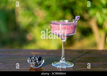 Frullato di mirtilli fresco in vetro di cristallo vintage sullo sfondo del giardino estivo su un tavolo di legno, primo piano. Concetto di mangiare sano. Frullati Foto Stock