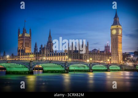 Vista del Big Ben e delle Houses of Parliament di Londra durante l'ora blu, con il Westminster Bridge in primo piano e riflessioni sul Tamigi R. Foto Stock