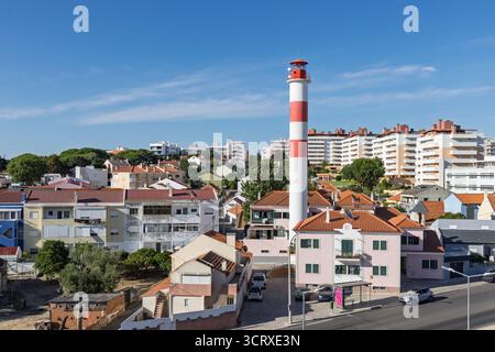 Una caratteristica torre del faro a strisce rosse e bianche si erge in mezzo a una vibrante area residenziale mista di Setúbal, con case colorate e un luminoso complesso Foto Stock