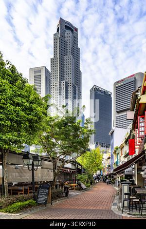 Vista di un vivace sentiero in mattoni rossi che conduce attraverso edifici colorati e lussureggianti alberi verdi verso i grattacieli torreggianti, Singapore, Singapore. Foto Stock