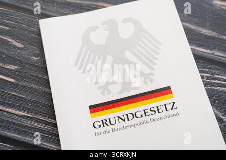 Baviera, Germania - 3 ottobre 2025: La legge fondamentale della Repubblica federale di Germania come libro stampato con aquila federale e bandiera tedesca su un tavolo di legno *** Das Grundgesetz der Bundesrepublik Deutschland als gedrucktes Buch mit Bundesadler und deutscher Flagge auf einem Holztisch Foto Stock