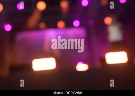 Le luci rosa, viola e arancione illuminano un palco durante un concerto. Il palcoscenico è sfocato, creando un'atmosfera astratta ed energica. Spotli Foto Stock