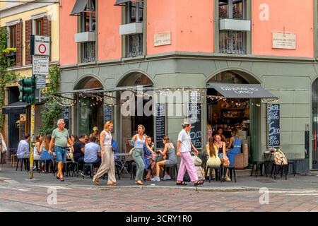 Le persone sedute fuori sul marciapiede si godono un drink al DeAmicis uno, un cocktail e un aperitivo bar in via Edmondo de Amicis, Milano, Italia Foto Stock