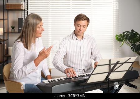 Tutore che insegna all'uomo a suonare il pianoforte al chiuso Foto Stock