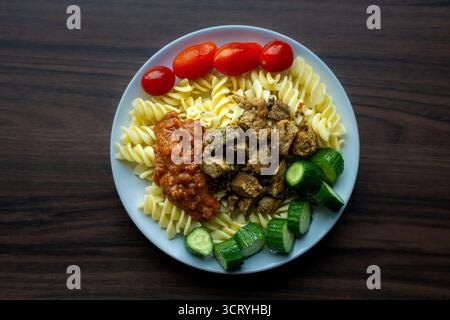 Insalata di pasta Fusilli con cetrioli pomodori ciliegini carne e salsa di pomodoro su piatto piatto colorato fatto in casa. Foto Stock