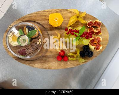Vista dall'alto verso il basso di un dessert gourmet e un piatto di frutta su una tavola di legno. Una bella disposizione di frutti di bosco freschi, fichi, uva e pasticcini, perfetta Foto Stock