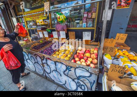 Donna cinese che tiene un sacchetto rosso al banco frutta con mele pere prugne e arance contro il negozio cinese. New York. STATI UNITI. Foto Stock