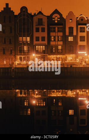 Danzica, Polonia – 27 febbraio 2025: Riflesso caldo dell'architettura storica di notte, facciate illuminate rispecchiate nelle calme acque del fiume Motlawa, ev Foto Stock