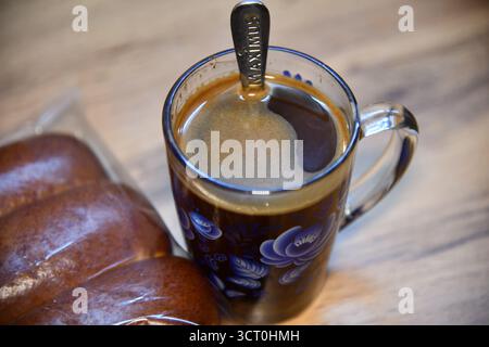 Miele dorato che gocciola dal cucchiaio nel recipiente marrone per il tè allo zenzero su un tavolo di legno Foto Stock
