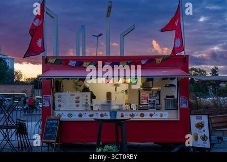 Il camion del cibo di strada nepalese Momo Haus serve gnocchi all'Europaplatz di Berlino al crepuscolo con bandiere colorate e cielo. Foto Stock