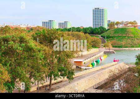 Cabecera Park a Valencia e lago adornato da vivaci pedalò, tra cui forme di cigno, circondato da alberi lussureggianti e da una prominente collina erbosa Foto Stock