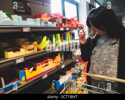 Lombardia, Italia - 1 ottobre 2025 Una donna in un negozio di alimentari a prezzi scontati in Italia esamina attentamente i prodotti su uno scaffale mentre spinge un carrello f Foto Stock