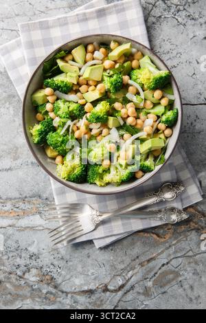 Insalata vegana con broccoli, ceci, avocado, cipolle ed erbe aromatiche da vicino in un recipiente sul tavolo. Vista dall'alto verticale Foto Stock