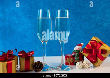 Composizione natalizia con bicchieri da champagne, scatole regalo e coni di pino sullo sfondo blu delle feste. Foto Stock