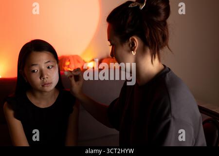 Un truccatore applica il trucco mistico a una ragazza per Halloween. Foto Stock