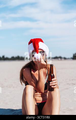 Donna con bikini e cappello di Babbo Natale che si rilassa sulla spiaggia tropicale durante le vacanze di Natale Foto Stock