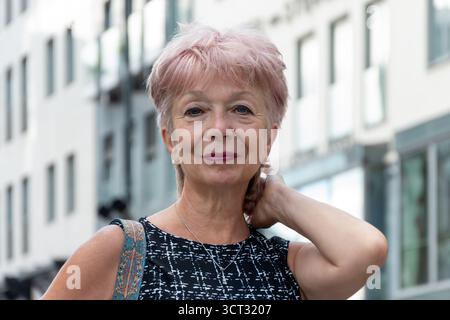 Un pensionato anziano, di 65 70 anni, si adatta i capelli mentre cammina per la città Foto Stock