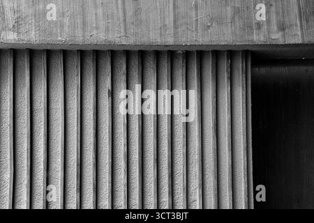 Un primo piano in bianco e nero che mostra le nervature verticali testurizzate e i motivi geometrici ruvidi di un moderno edificio in cemento dal design minimalista e brutale Foto Stock