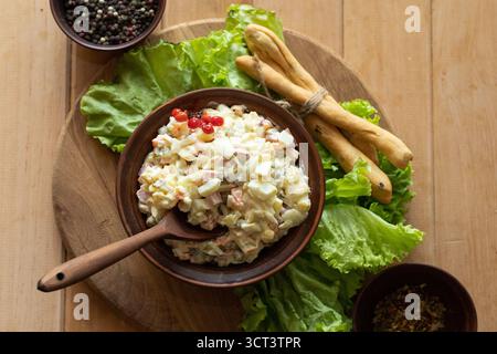 Insalata Olivier fatta in casa con verdure uova e maionese servita in un recipiente marrone con foglie di lattuga e grissini sfondo rustico naturale per il cibo Foto Stock