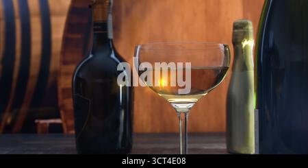 Un bel vetro semicircolare con alcol forte su uno sfondo di botti di rovere e bottiglie con alcool d'elite Foto Stock