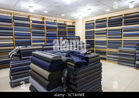 Abbigliamento in negozio, rotoli di tessuto e tessuti in vendita impilati sugli scaffali in negozio, vista di rotoli di tessuto di colori e motivi diversi sugli scaffali in Foto Stock