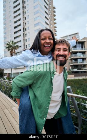 Coppia interrazziale che fa il piggyback e si diverte in città Foto Stock