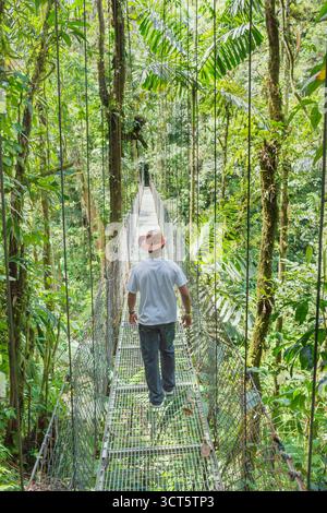 Uomo che cammina sul ponte sospeso nella foresta pluviale, la fortuna, provincia di Alajuela, Costa Rica Foto Stock