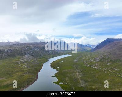 Veduta aerea di un lungo lago e fiume serpentino che si snodano attraverso un'ampia e verde valle d'alta quota circondata da montagne rocciose Foto Stock