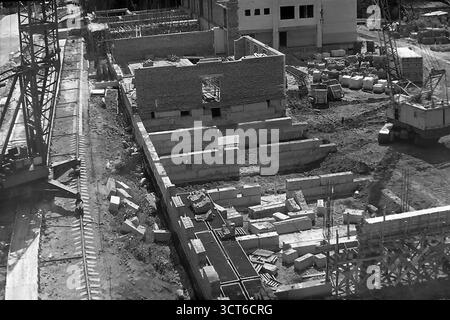 Una vista ad alto angolo di un importante cantiere a Sloviansk, RSS Ucraina, durante gli anni '1980 Questa fotografia d'archivio cattura lo sviluppo urbano nel tardo periodo sovietico, mostrando la fase iniziale di costruzione di quello che presumibilmente è un nuovo 'Univer-sam' (supermercato). Le fondamenta sono disposte con grandi blocchi di cemento e le prime pareti in mattoni sono in aumento. Torri e gru mobili dominano la scena, circondate da materiali da costruzione, che illustrano i metodi industriali dell'epoca. Questa immagine di creazione attiva simboleggia la crescita pacifica e la modernizzazione della città Foto Stock